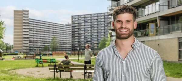 Man staand in park met flats op de achtergrond.