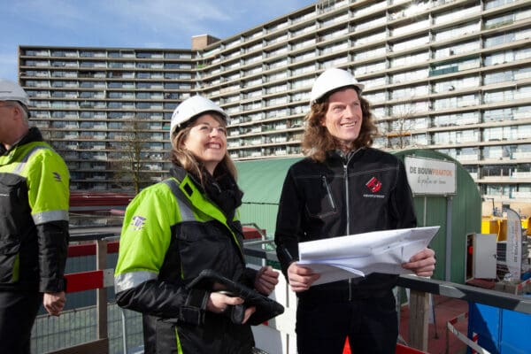 Man en vrouw staand met kaart in handen en bouwhelm op