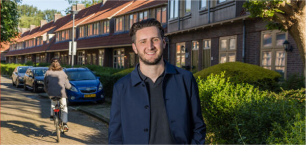 Man staand voor rijtjeswoningen met op de achtergrond enen vrouw op de fiets.