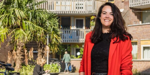 Vrouw met rood jasje staand voor gebouw