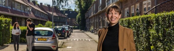 Vrouw staand in straat met rijtjeswoningen.