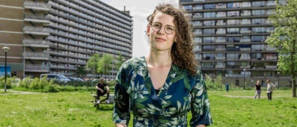 Vrouw met bril staand voor flatwoningen.